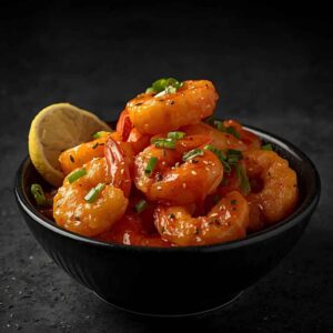 A bowl of crispy prawns tossed in creamy spicy dynamite sauce, garnished with spring onions and chilies, served as a bold seafood starter.